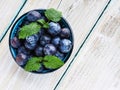 Fresh blueberries in blue bowl and leaves of mint on white wooden table Royalty Free Stock Photo