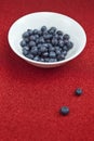 Fresh blueberries in a white bowl on red glittering background.
