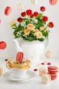 Fresh bouquet of roses, flying macarons and splashing tea on white background. Food levitation concept.