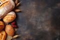 Fresh bread, buns, loaves, rolls, wheat ears on rustic black wooden background, text copy space, top view, flat lay