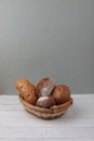 Fresh bread in a wicker basket on wooden table against gray background. Vertical image