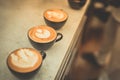 Fresh brewed coffees with beautiful latte art on surface, three cup in a row on wooden table ready to drink Royalty Free Stock Photo