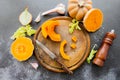 Fresh bright cutted pumpkin on a wooden chopping board with knife. Celery and garlic, onions and scattered peppercorns and salt