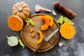 Fresh bright cutted pumpkin on a wooden chopping board with a knife. Celery and garlic, onions and scattered peppercorns and salt