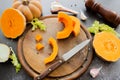 Fresh bright cutted pumpkin on a wooden chopping board with a knife. Celery and garlic, onions and scattered peppercorns and salt