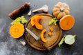 Fresh bright cutted pumpkin on a wooden chopping board with knife. Celery and garlic, onions and scattered peppercorns and salt