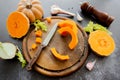 Fresh bright cutted pumpkin on a wooden chopping board with knife. Celery and garlic, onions and scattered peppercorns and salt