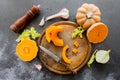 Fresh bright cutted pumpkin on a wooden chopping board with a knife. Celery and garlic, onions and scattered peppercorns and salt