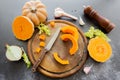 Fresh bright cutted pumpkin on a wooden chopping board with a knife. Celery and garlic, onions and scattered peppercorns and salt