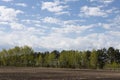 Fresh bright spring landscape in outdoors with fluffy clouds in blue heaven with sunlight above black field of arable land. Royalty Free Stock Photo