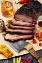 Fresh Brisket BBQ beef sliced for serving against a kraft paper background with sauce, hot peppers and corn.