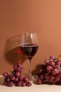 Fresh bunch of grapes with glass of tasty red wine on beige background with shadow on the wall. Wine time. Food concept