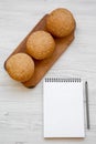 Fresh burger buns with sesame seeds on wooden board and blank notepad on white wooden background, overhead view. Flat lay, from ab Royalty Free Stock Photo