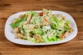 Fresh caesar salad with chicken pieces served on white dish on wooden background. Royalty Free Stock Photo