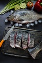 Fresh carp on a dark background with greens and vegetables. Cut into pieces carp on a wooden board Royalty Free Stock Photo