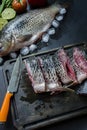 Fresh carp on a dark background with greens and vegetables. Cut into pieces carp on a wooden board Royalty Free Stock Photo