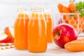 Fresh carrot and apple juice on white background. Carrot and apple juice in glass bottles on white table, closeup Royalty Free Stock Photo