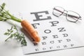 Fresh carrots as a source of vitamin A placed on the eye test chart. Glasses and carrot, concept of good eyesight