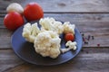 Fresh cauliflower and cherry tomatoes on a brown round plate on a wooden surface Royalty Free Stock Photo