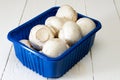 Fresh champignons in blue box on white wooden background