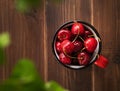Fresh cherries in a red mug on a dark wooden background with leaves close up. The concept of rustic style. Top view Royalty Free Stock Photo