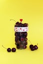 Fresh cherry berries in a glass jug isolated on a yellow background