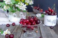 Fresh cherry fruit in glass vase, other dishes with berries and jar with jasmine and wildflowers on the old wooden table. Soft sel Royalty Free Stock Photo