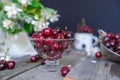 Fresh cherry fruit in glass vase, other dishes with berries and jar with jasmine and wildflowers on the old wooden table. Soft sel Royalty Free Stock Photo