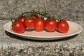 Fresh cherry tomatoes on white plate across natural stone background. Close-up. Salad ingredient. Cuisine. Healthy food concept