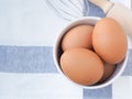 Fresh chicken eggs in a white bucket and whisk, rolling pin on a white dishcloth with blue straight stripes.