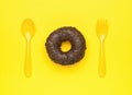 Fresh chocolate donut, yellow spoon and fork on a yellow background. The minimal concept of popular baking