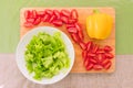 Fresh chopped green lettuce leaves lie on a wooden cutting board next to the yellow bell pepper and chopped red cherry Royalty Free Stock Photo