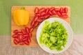 Fresh chopped green lettuce leaves lie on a wooden cutting board next to the yellow bell pepper and chopped red cherry Royalty Free Stock Photo