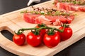 chopped raw pork steaks with seasoning, ripe tomatoes and thyme on a cutting kitchen board on a black wooden table Royalty Free Stock Photo