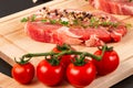 Chopped raw pork steaks with seasoning, ripe tomatoes and thyme on a cutting kitchen board on a black wooden table Royalty Free Stock Photo