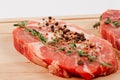 Fresh chopped raw pork steaks with spices and thyme on a cutting kitchen board on a white table Royalty Free Stock Photo
