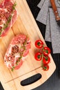 fresh chopped raw pork steaks with spices, tomatoes and thyme on a cutting kitchen board on a black wooden table Royalty Free Stock Photo