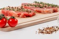 Chopped raw pork steaks with spices, tomatoes and thyme on a cutting kitchen board on a white wooden table Royalty Free Stock Photo