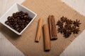 Cinnamon, star anise, coffee beans grouped together on a hessian cloth with a light wood background