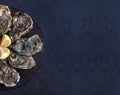 Fresh closed oysters with lemon on black plate on dark grey background