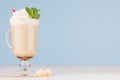 Fresh coffee drink with whipped cream, green mint, straw, cookies in irish coffee glass on soft light blue wall and white wooden.