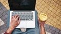 Fresh coffee. Top view of man working on laptop and holding cup of coffee while sitting outdoors Royalty Free Stock Photo