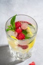 Fresh cold ice water drink with lemon, raspberry fruits and mint leaf in faceted glass on stone concrete background Royalty Free Stock Photo