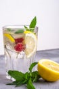 Fresh cold ice water drink with lemon, raspberry fruits and mint leaf in faceted glass on stone concrete background Royalty Free Stock Photo