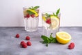 Fresh cold ice water drink with lemon, raspberry fruits and mint leaf in two faceted glass on stone concrete background Royalty Free Stock Photo