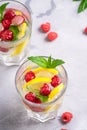 Fresh cold ice water drink with lemon, raspberry fruits and mint leaf in two faceted glass on stone concrete background Royalty Free Stock Photo