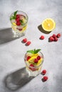 Fresh cold ice water drink with lemon, raspberry fruits and mint leaf in two faceted glass on stone concrete background Royalty Free Stock Photo