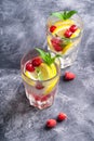 Fresh cold ice water drink with lemon, raspberry fruits and mint leaf in two faceted glass on stone concrete background Royalty Free Stock Photo