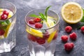 Fresh cold ice water drink with lemon, raspberry fruits and mint leaf in two faceted glass on stone concrete background Royalty Free Stock Photo