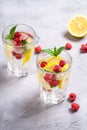 Fresh cold ice water drink with lemon, raspberry fruits and mint leaf in two faceted glass on stone concrete background Royalty Free Stock Photo